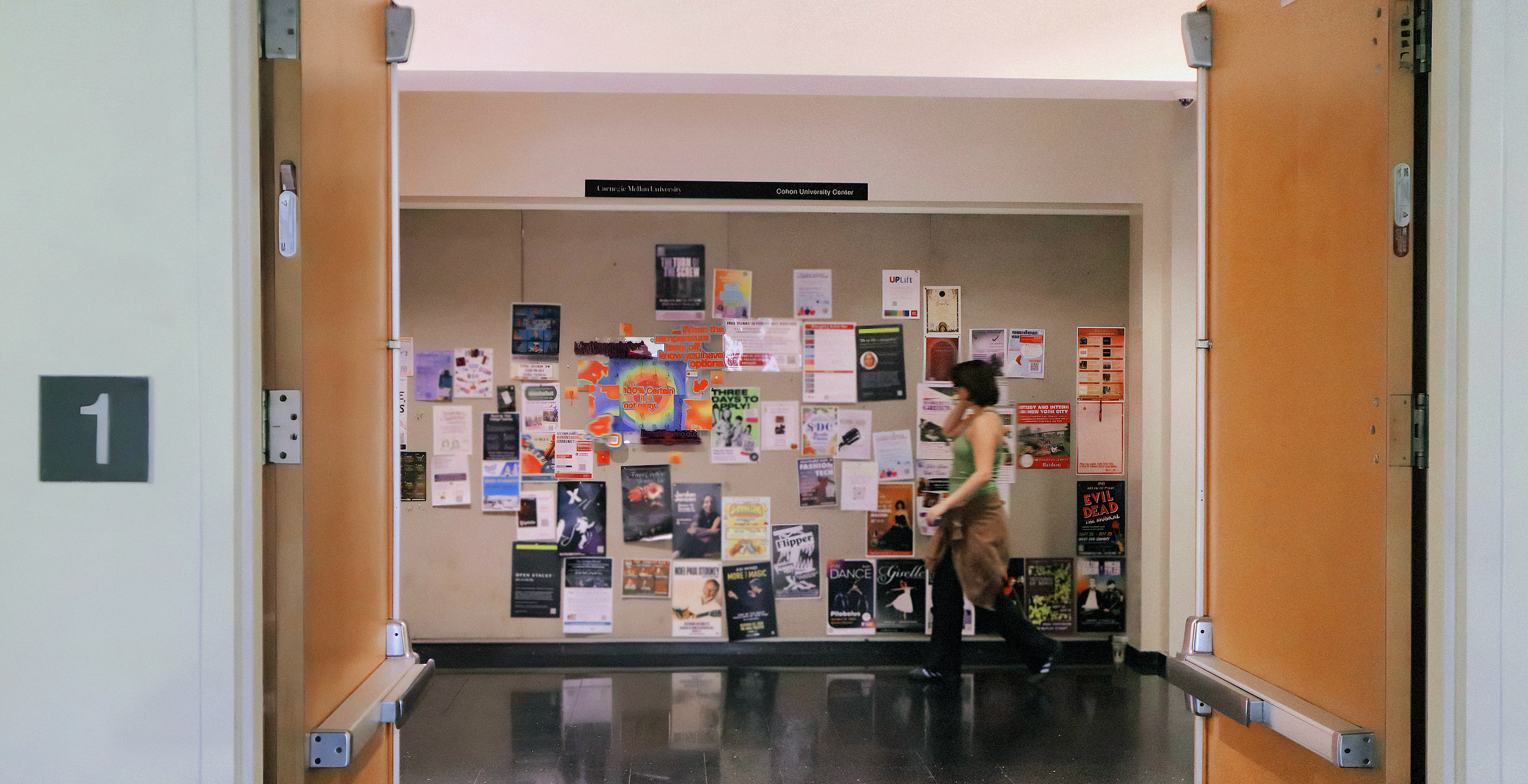 The installation seen through the doors of the University Center, on the central bulletin board as a student walks past
